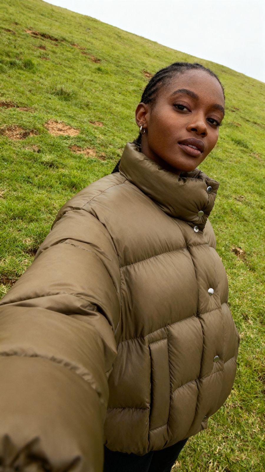 a woman in a puffy coat standing on a grassy hill