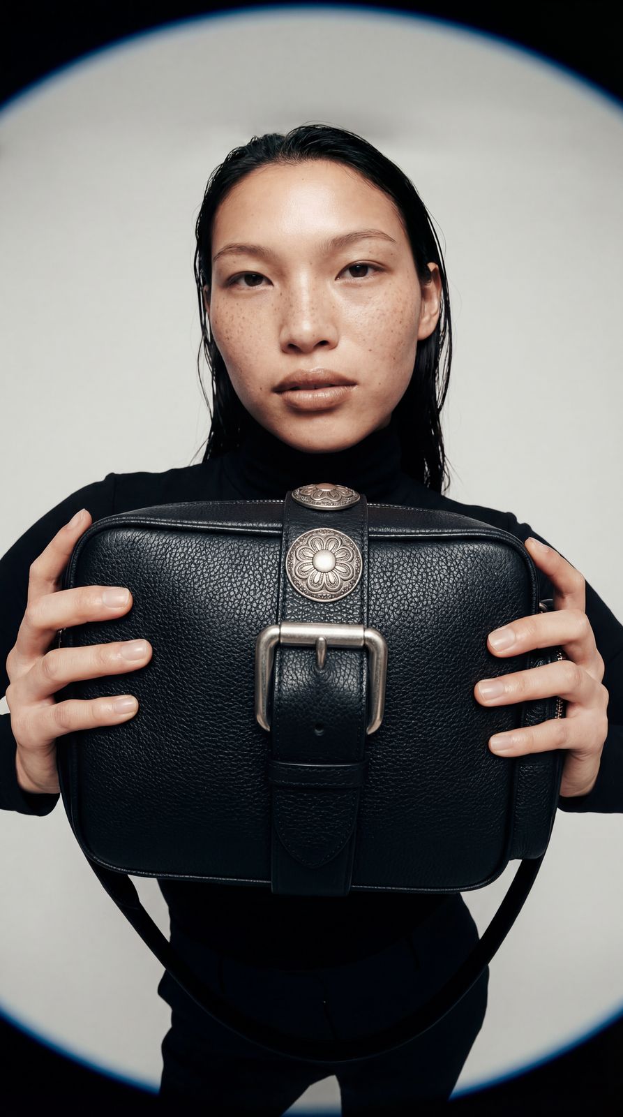 a woman holding a black purse in front of her face
