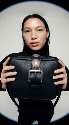 a woman holding a black purse in front of her face