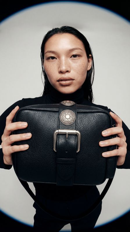 a woman holding a black purse in front of her face