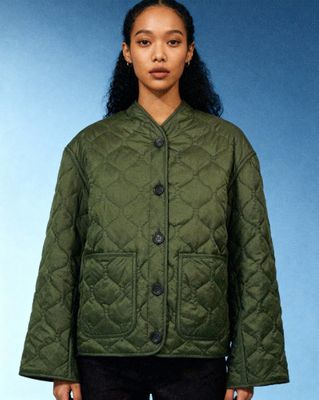 a woman standing in front of a blue background wearing a green jacket