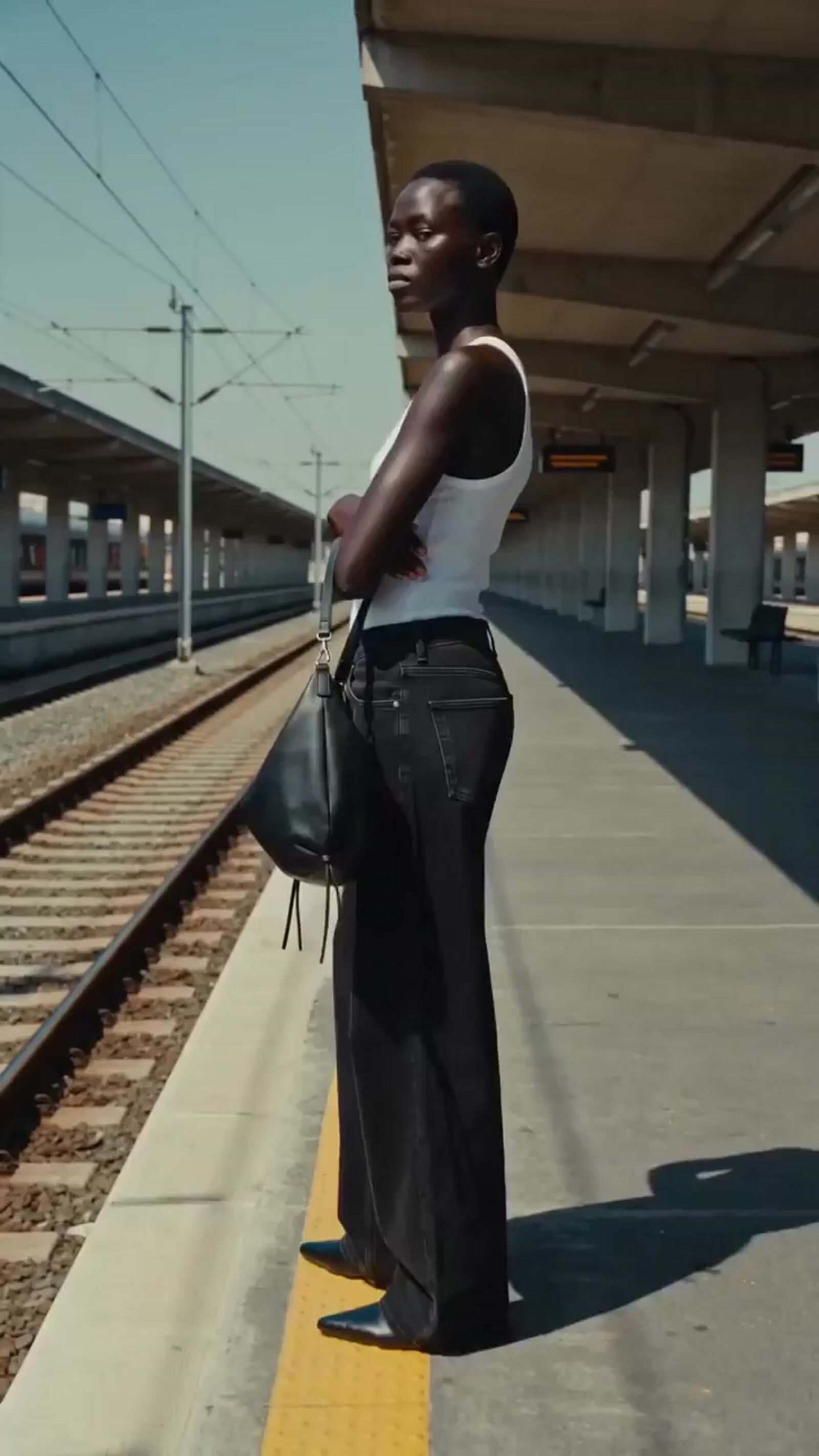 a woman standing on a train platform holding a purse