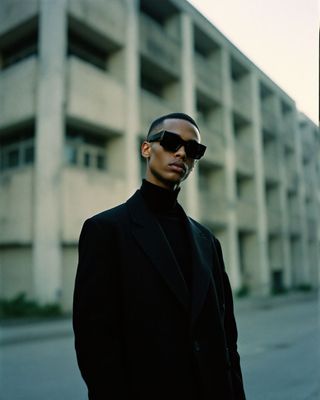 a man in a suit and sunglasses standing in front of a building