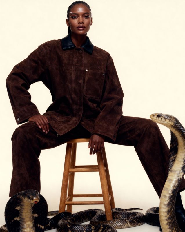 a woman sitting on a stool next to two snakes