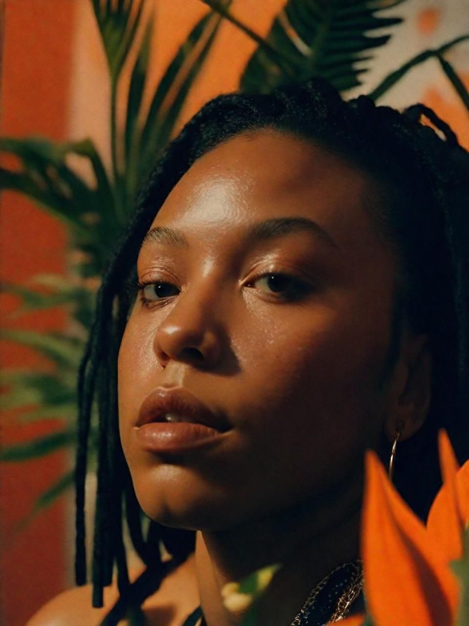 a woman with dreadlocks standing in front of a plant