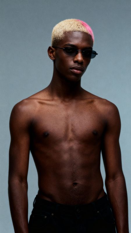 a man with a pink mohawk standing in front of a gray background