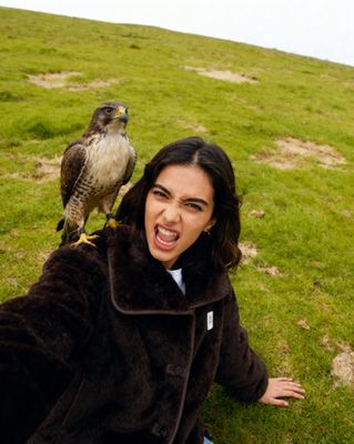 a woman sitting on the ground with a bird on her shoulder