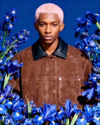 a man with pink hair standing in a field of blue flowers