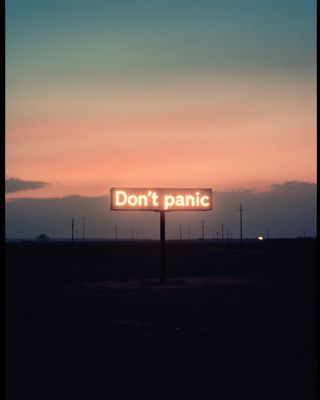 a sign that says don't panic in front of a sunset