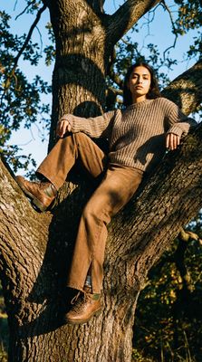 a man sitting in a tree wearing a sweater and pants
