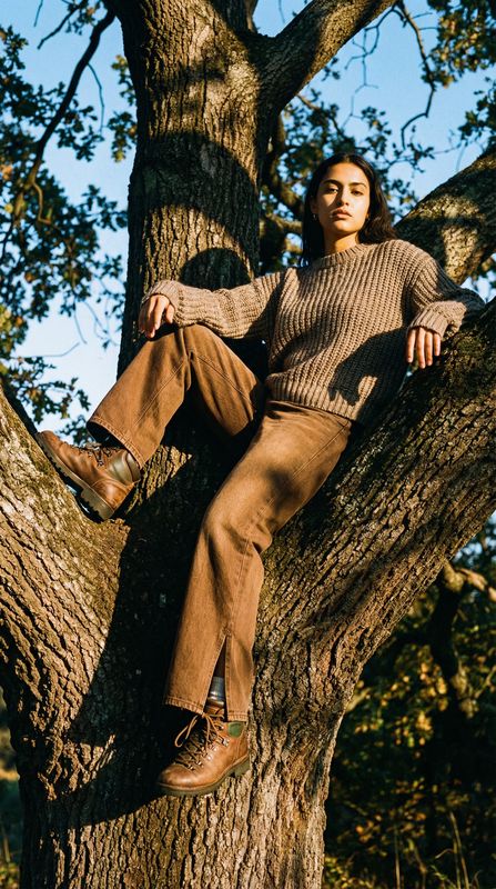 a man sitting in a tree wearing a sweater and pants