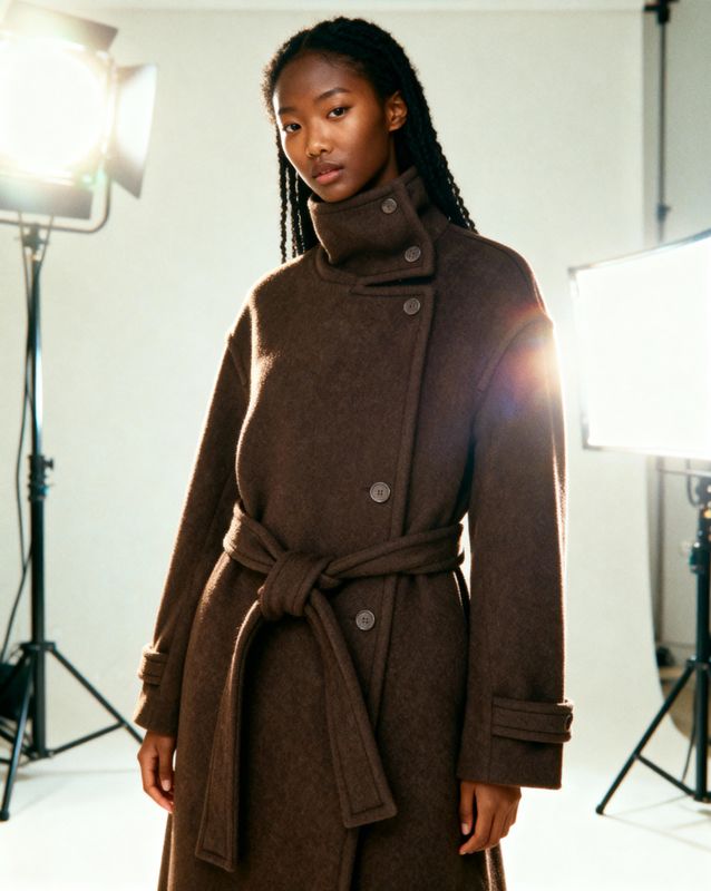 a woman in a brown coat standing in front of a camera
