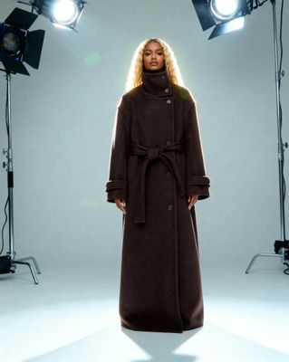 a woman in a brown coat standing in front of lights