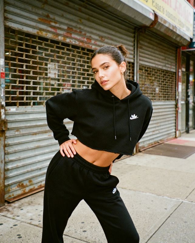 a woman standing on a sidewalk wearing a black hoodie and sweatpants