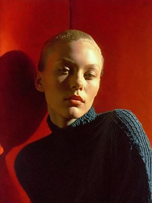 a woman in a black turtle neck sweater standing in front of a red wall