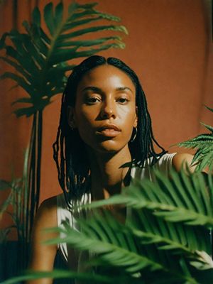 a woman with dreadlocks standing in front of a plant