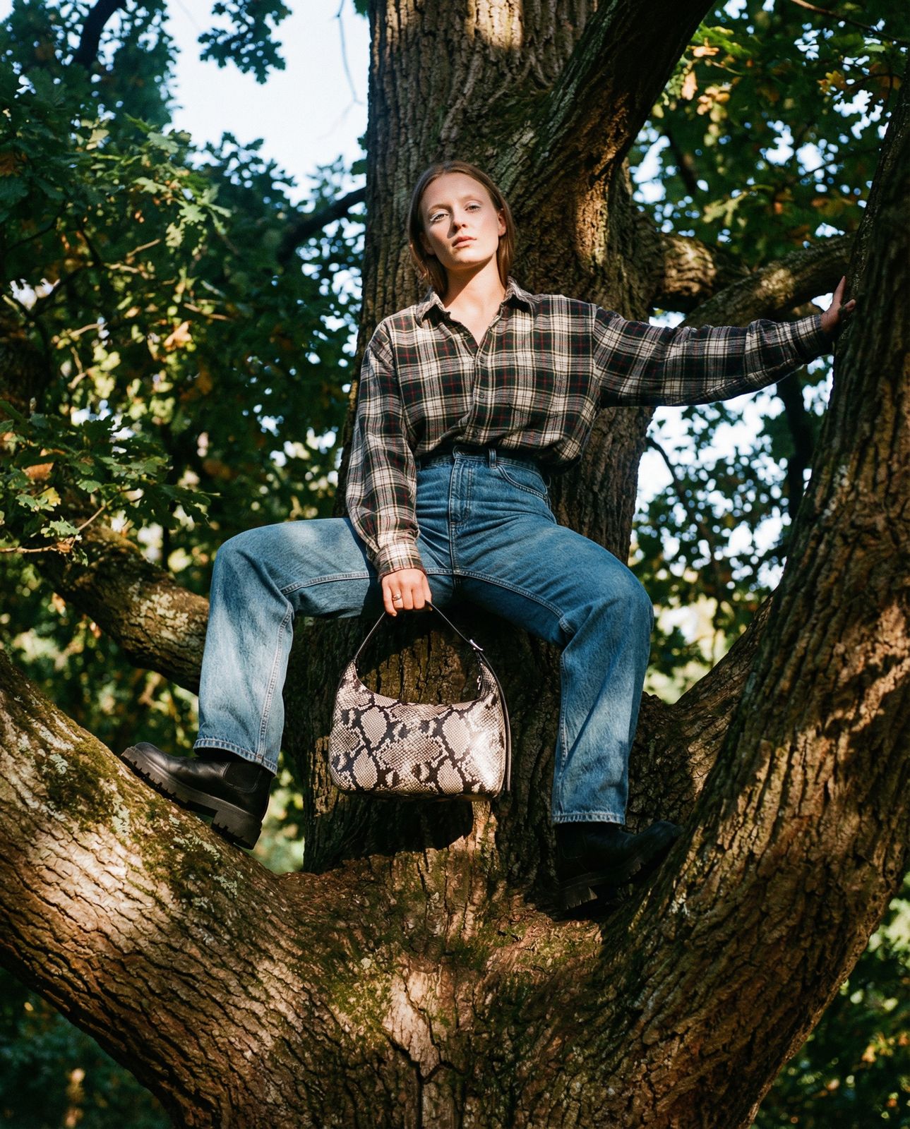a woman sitting in a tree with a handbag