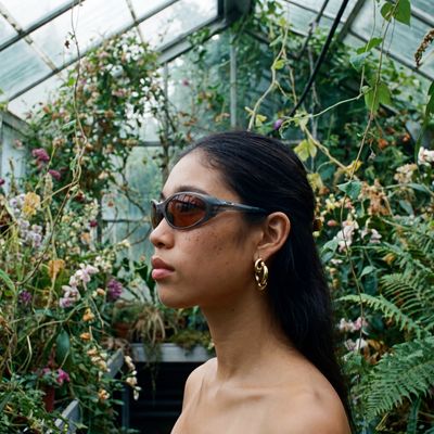a woman wearing sunglasses standing in front of a greenhouse