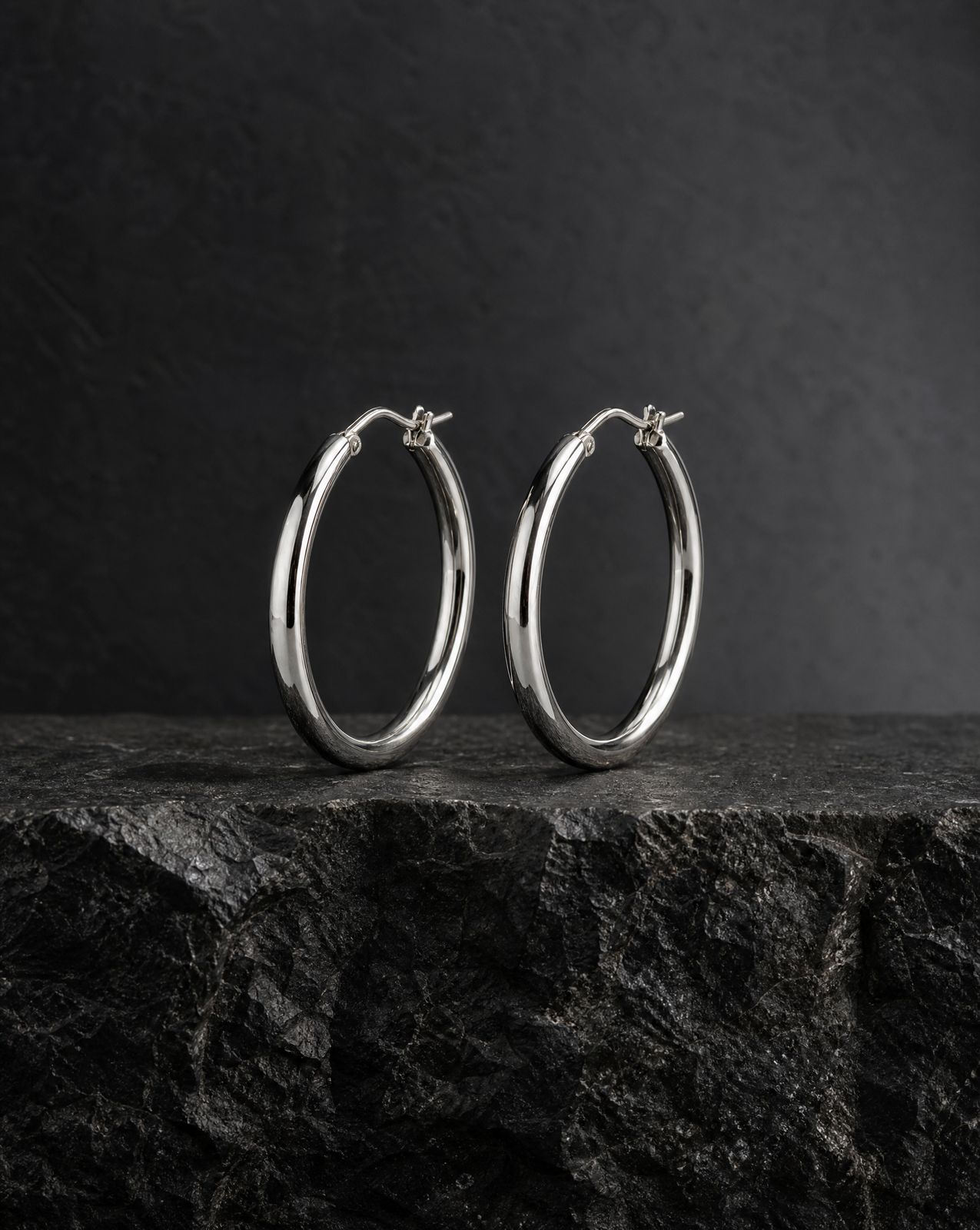 a pair of silver hoop earrings sitting on top of a rock