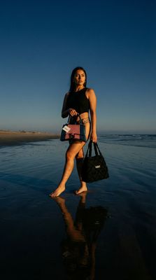 a woman walking on the beach with a handbag