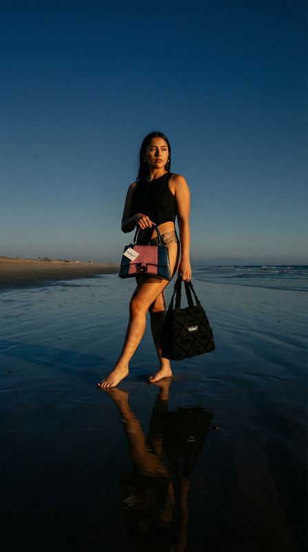 a woman walking on the beach with a handbag