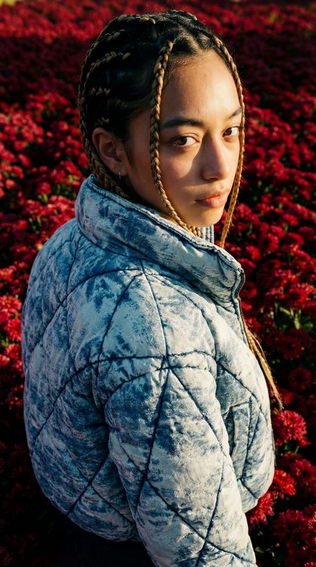 a woman with braids standing in a field of flowers