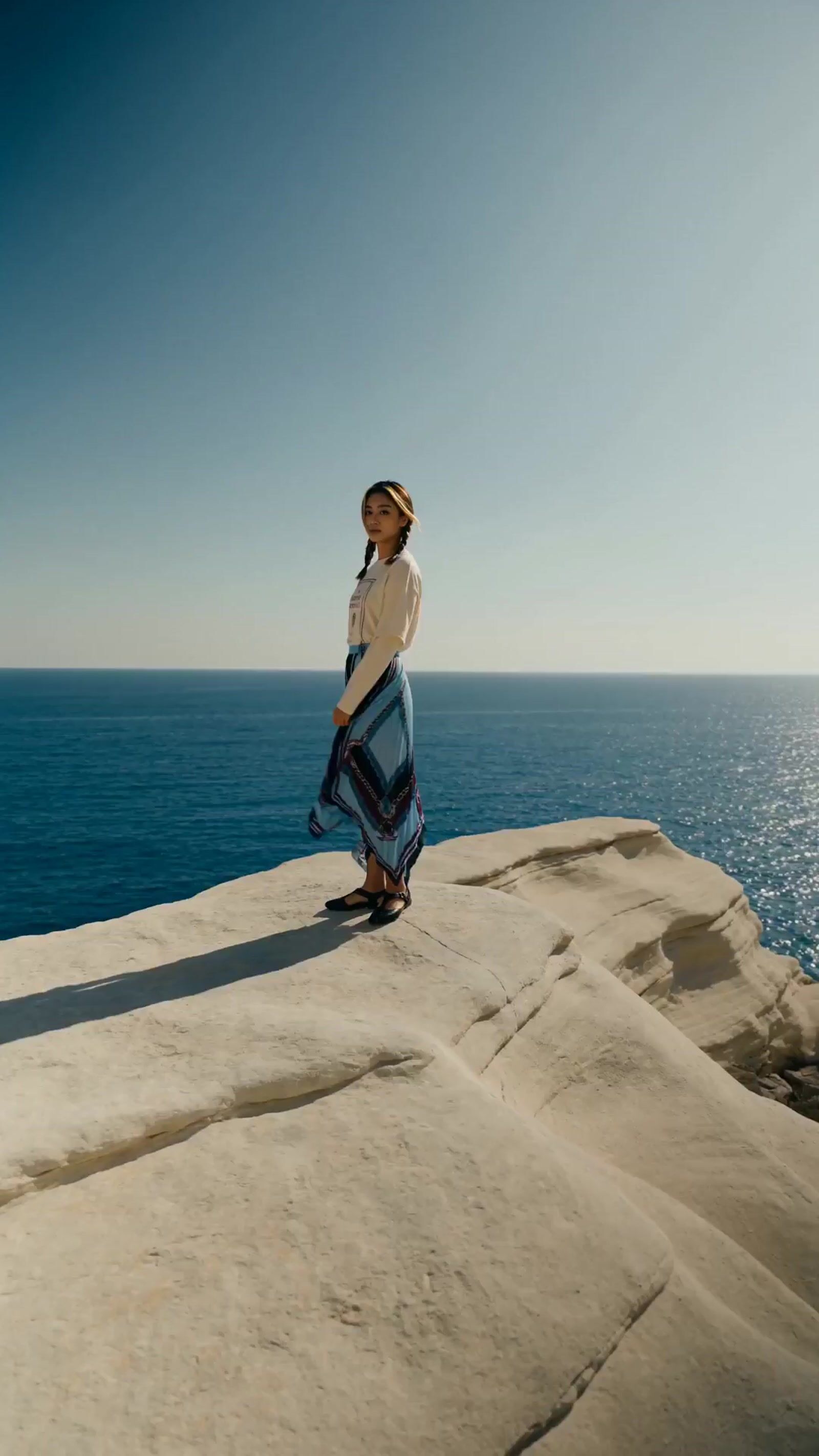a woman standing on top of a rock next to the ocean