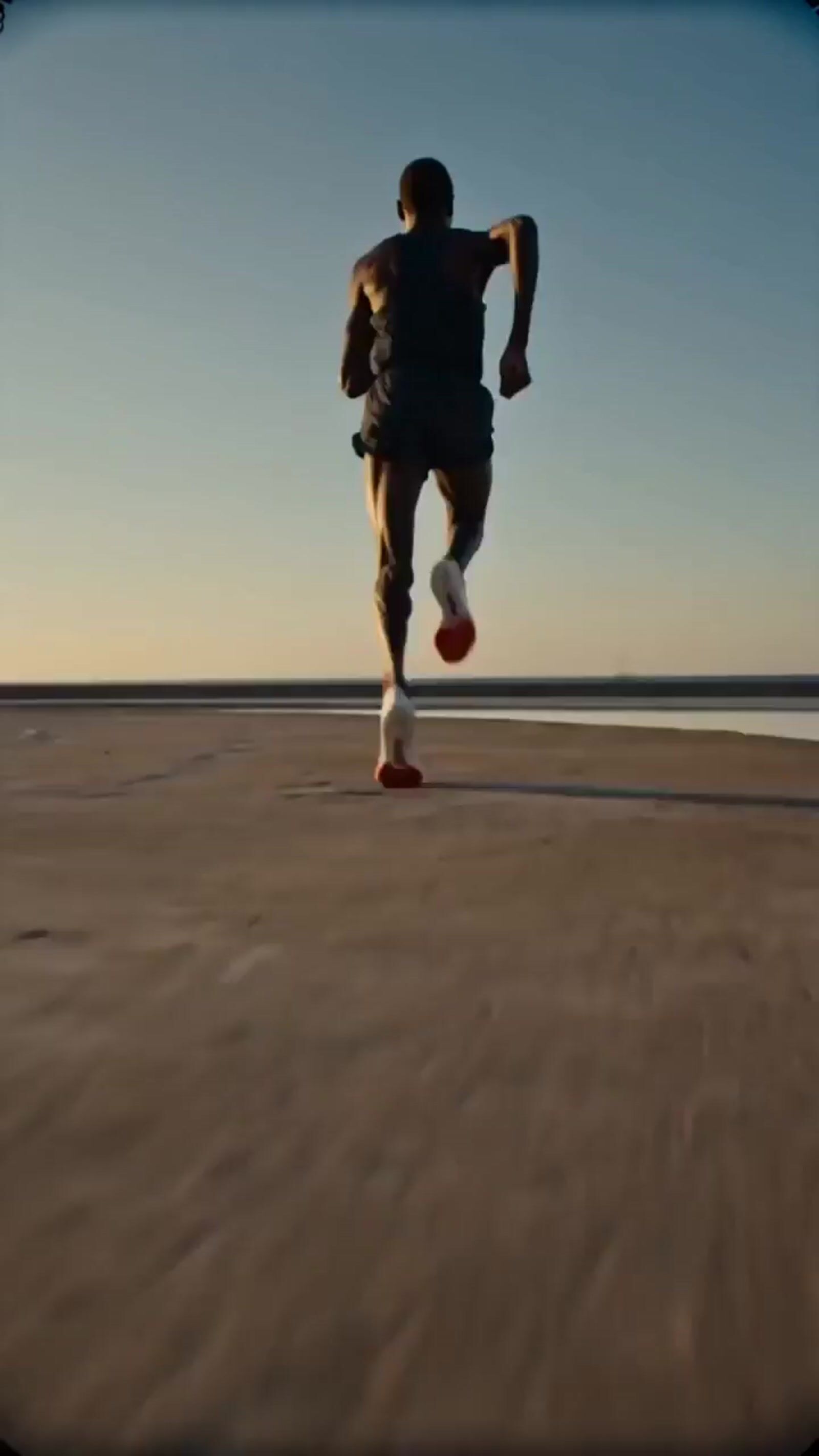 a man running across a sandy beach under a blue sky