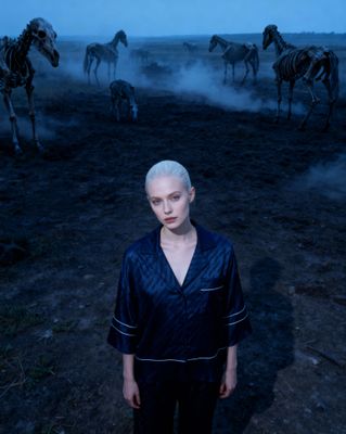 a woman with white hair standing in front of a herd of zebras
