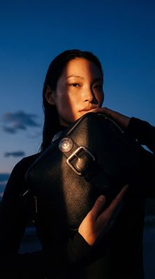 a woman holding a black purse in front of her face