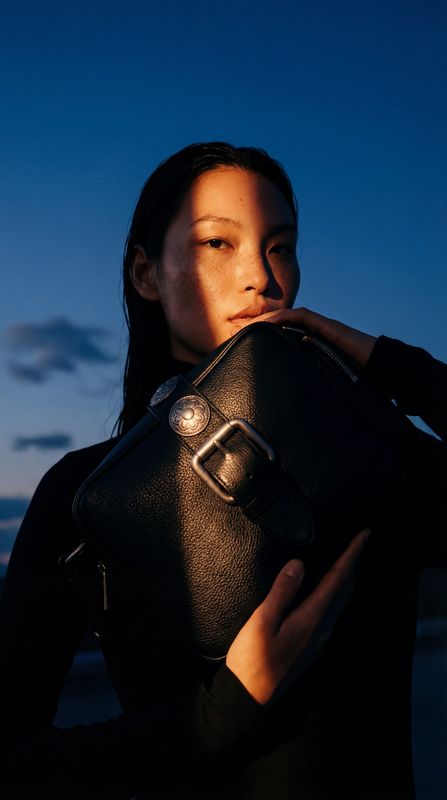 a woman holding a black purse in front of her face