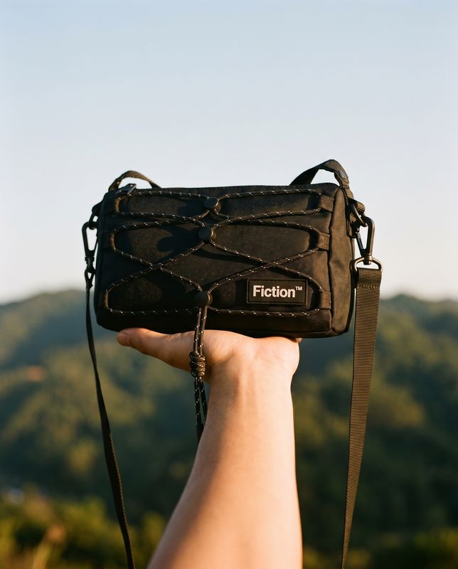 a hand holding a black camera bag over a mountain