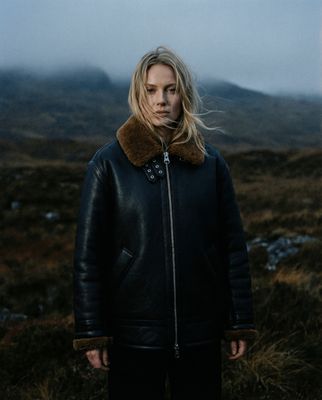 a woman standing in a field with a mountain in the background