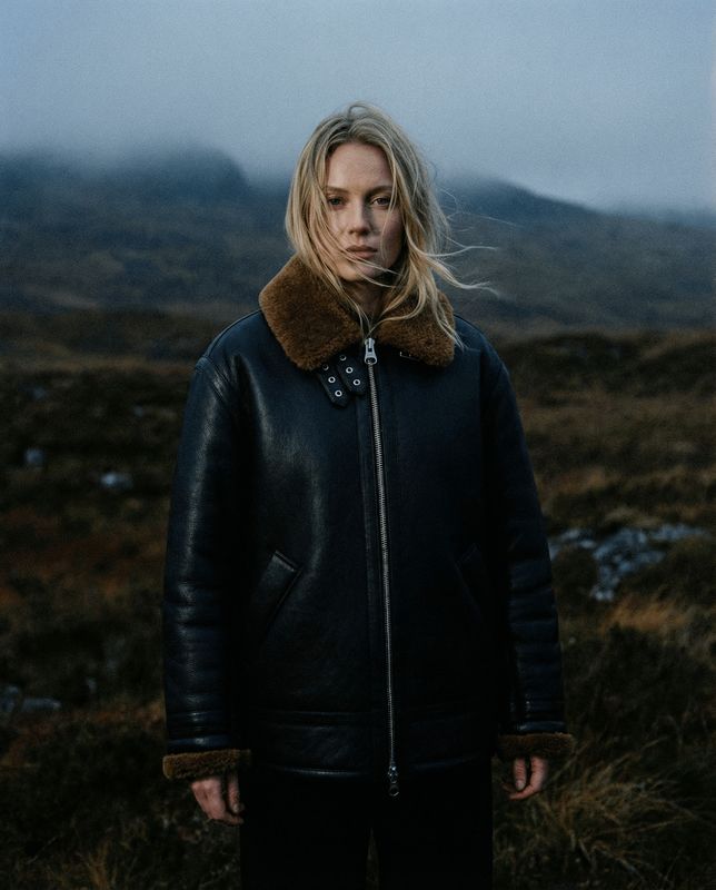 a woman standing in a field with a mountain in the background
