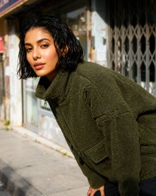 a woman in a green jacket leaning against a wall