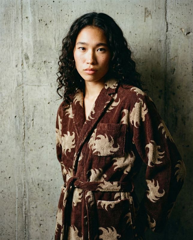 a woman wearing a robe standing in front of a concrete wall
