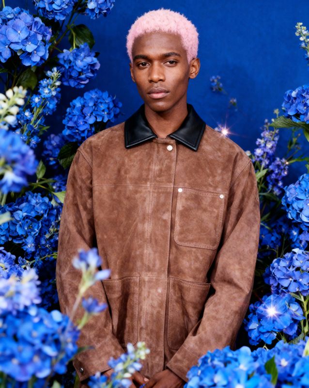a man with pink hair standing in front of blue flowers