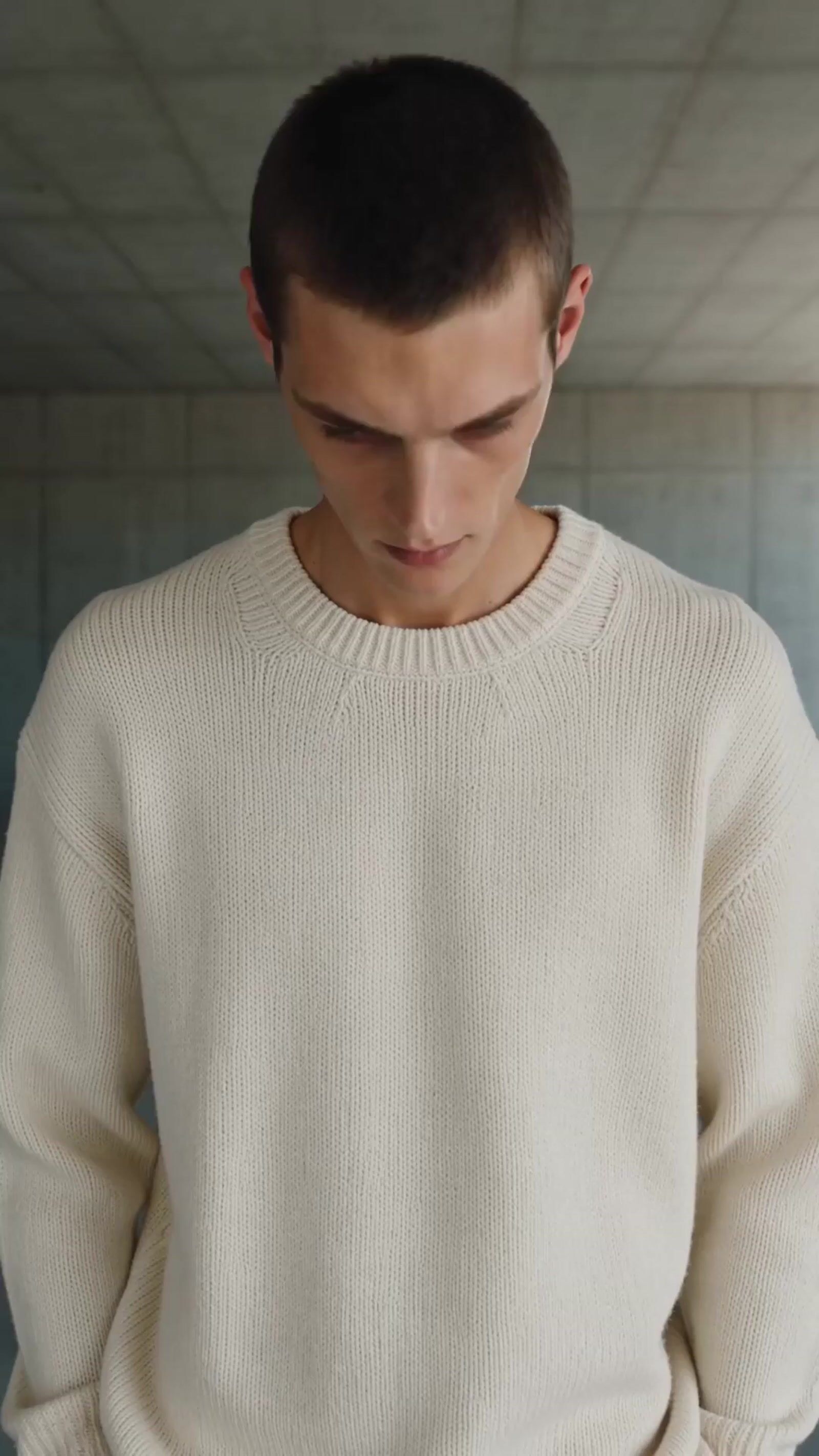 a man in a white sweater looking down at his cell phone