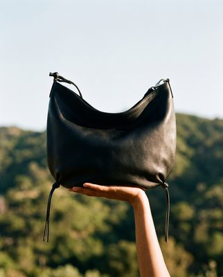 a hand holding a black purse in front of a mountain