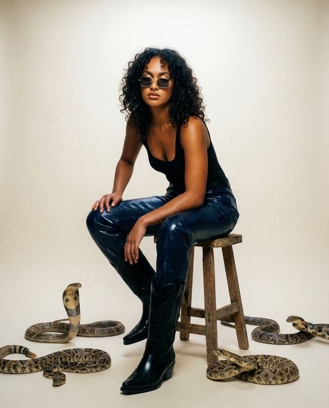 a woman sitting on a stool with snakes around her