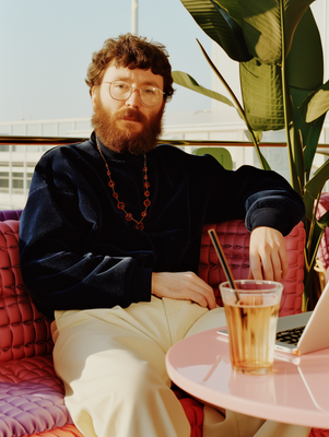 a man with a beard sitting at a table with a drink in front of him