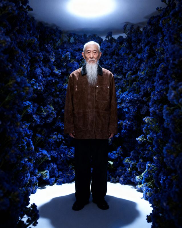 a man with a long white beard standing in front of blue flowers
