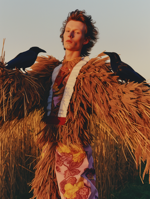 a woman standing in a field with two birds on her shoulders