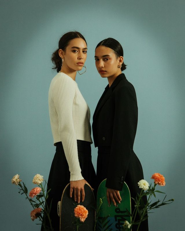 two women standing next to each other holding a skateboard