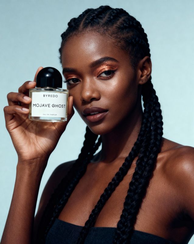 a woman with braids holding a bottle of perfume