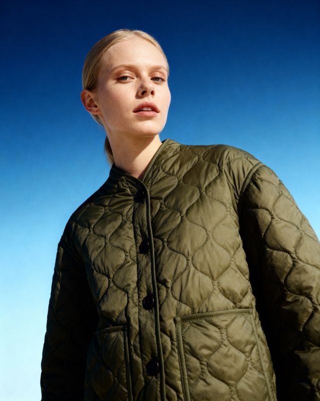 a woman in a green jacket standing in front of a blue sky