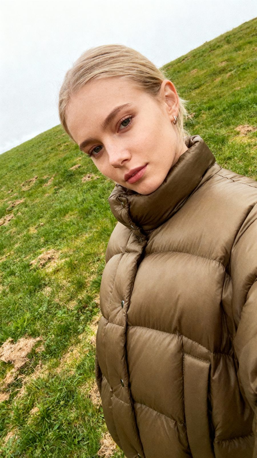 a woman in a puffy coat standing on a grassy hill