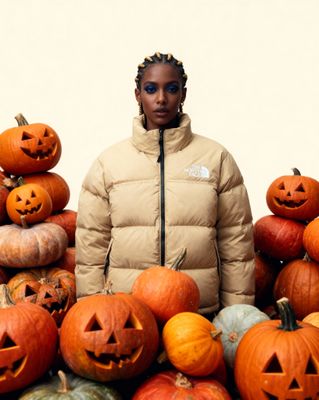 a woman standing in front of a pile of pumpkins