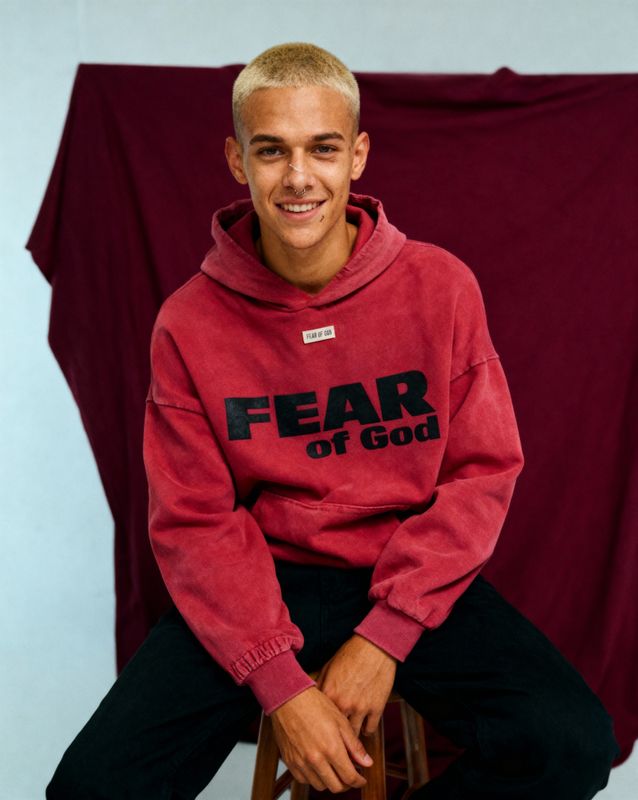 a young man sitting on a stool wearing a red hoodie