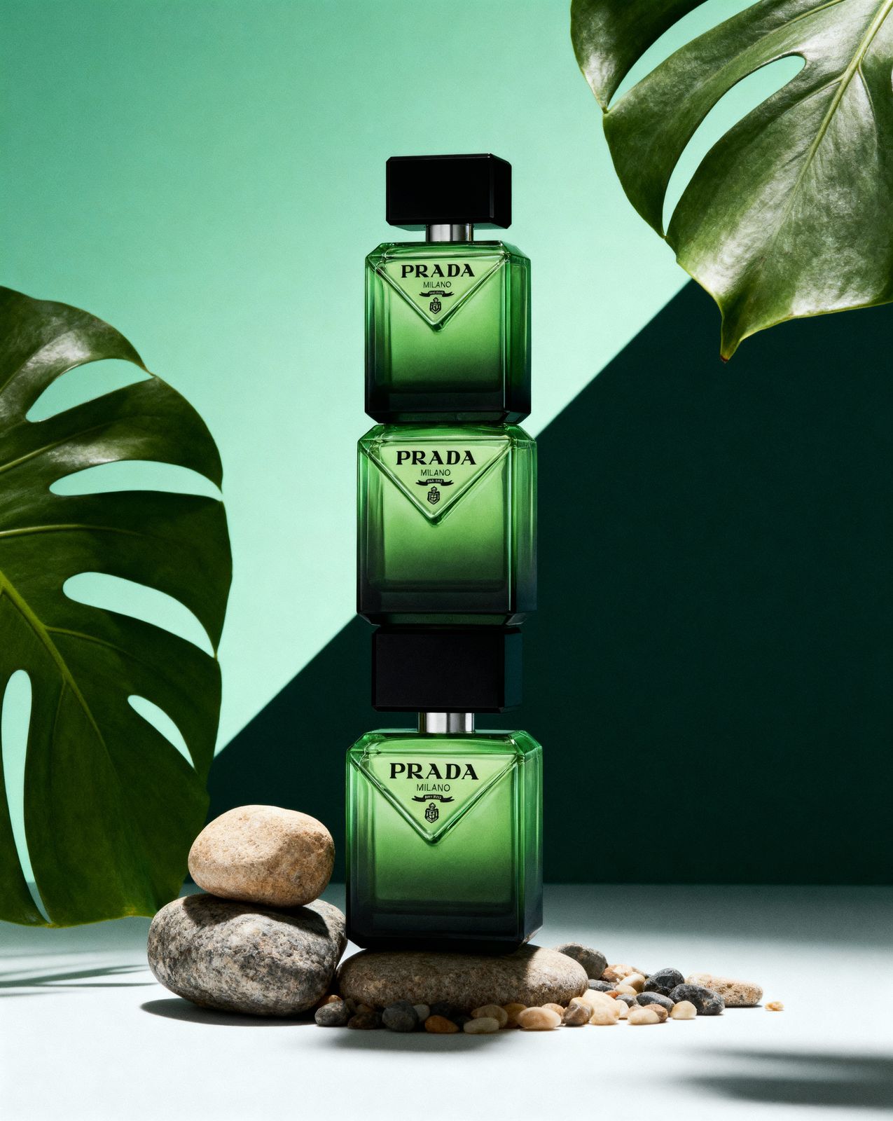 a green bottle of prada next to some rocks and a plant